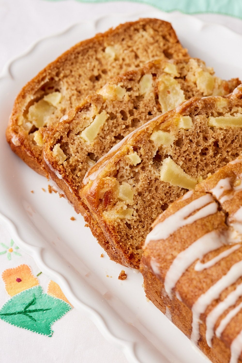 Apple Loaf Cake9 Slices of moist Apple Loaf Cake packed with diced apples and warm cinnamon, topped with a simple apple glaze on a white platter.