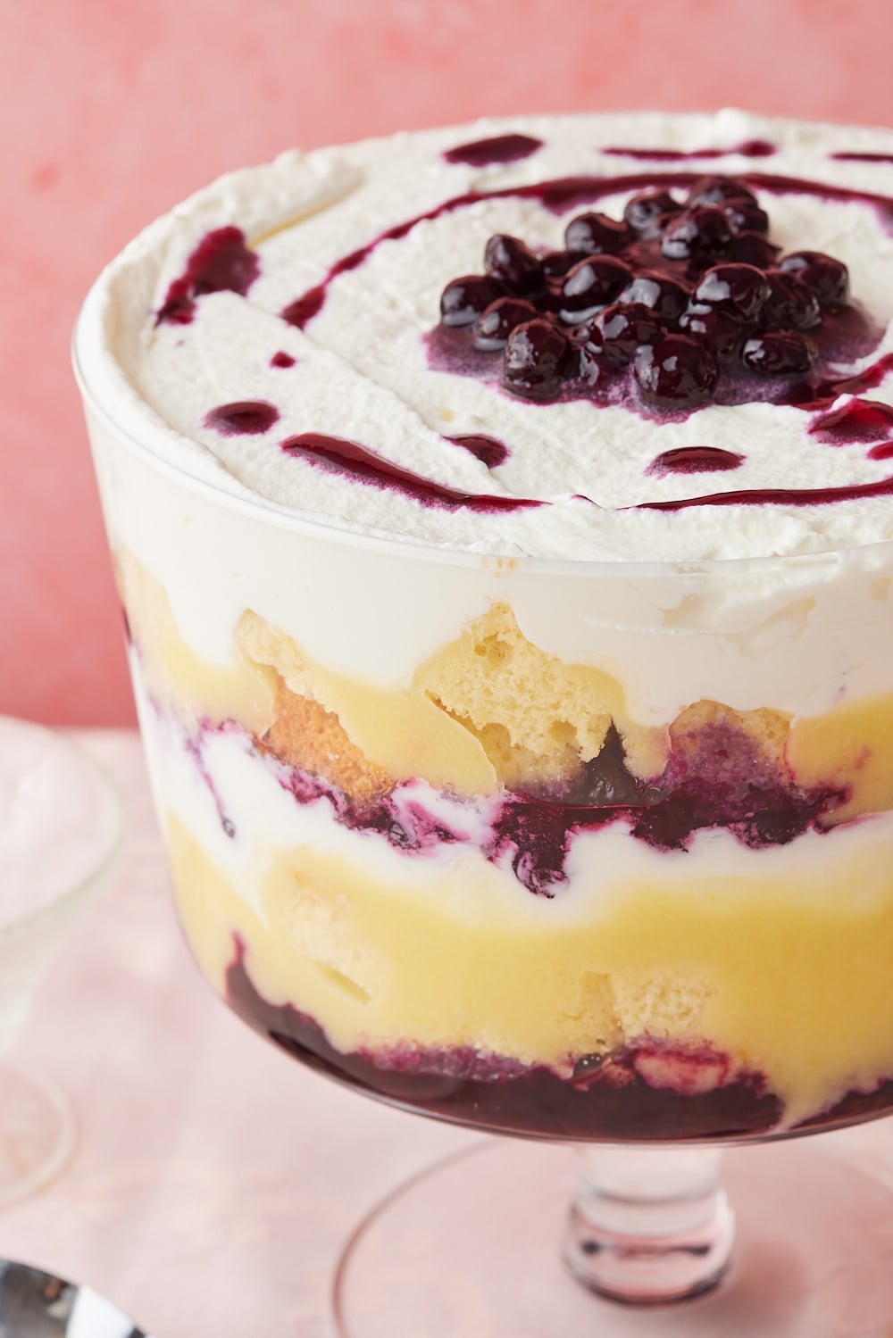 A close-up shot from the side of Lemon Blueberry Truffle shows the layers of blueberry filling, cake, whipped cream, and lemon curd. Topped with more blueberries.