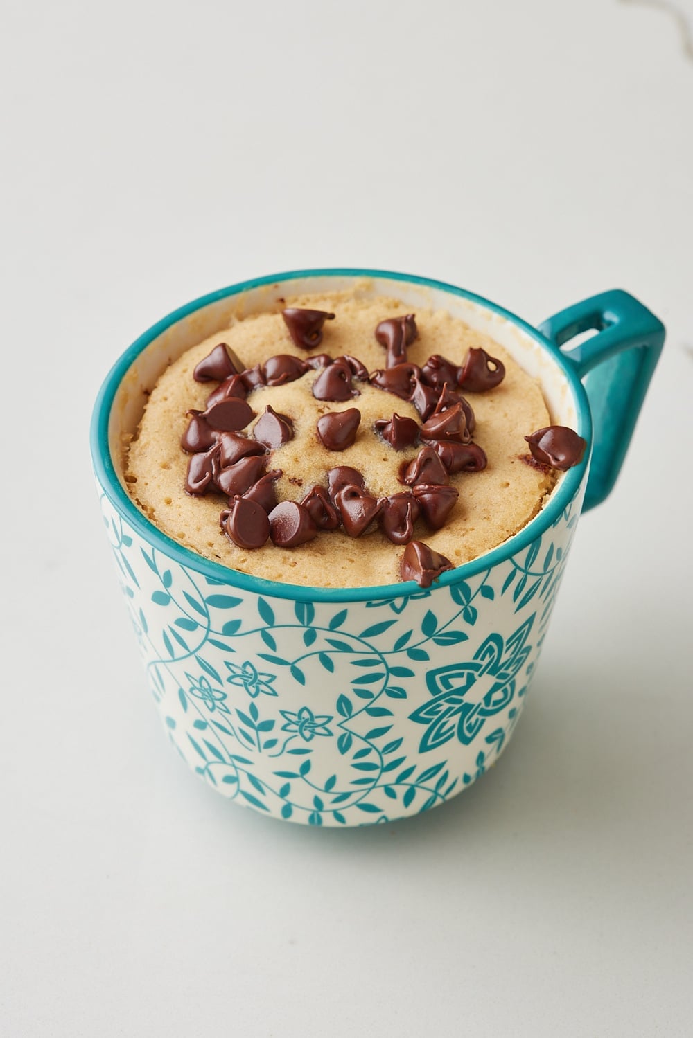 Chocolate chip mug cake in a teal floral mug. 