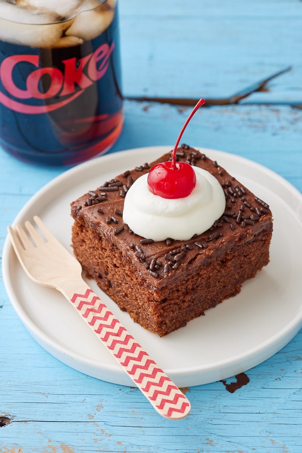 Coca Cola Cake16 A square of Coca Cola Cake served with whipped cream and cherry on top, with a can of coke on the side.
