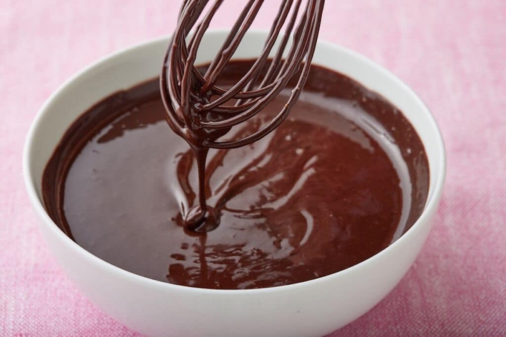 Silky thick hot fudge sauce dripping from the whisk into a bowl.