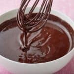 Silky thick hot fudge sauce dripping from the whisk into a bowl.
