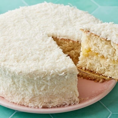 Pineapple Coconut Cake coated with shredded coconut, with one slice cut, showing the moist crumbs.