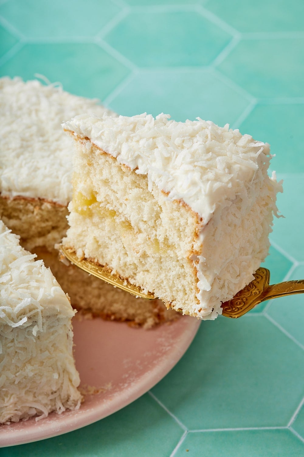 Pineapple Coconut Cake17 Pineapple Coconut Cake coated with shredded coconut, with one slice cut, showing the moist crumbs.
