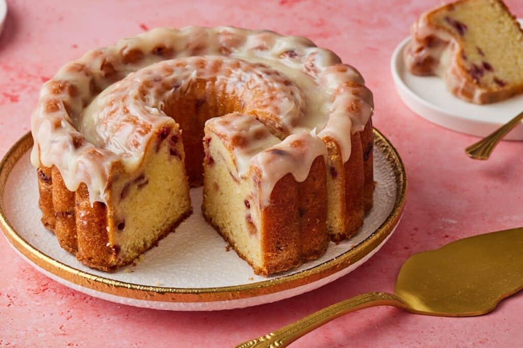 A glazed Strawberry Lemon Pound Cake with one slice cut and served on the side.