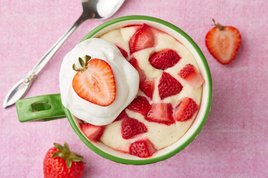 Top-down view of strawberry shortcake mug cake with fresh strawberries and whipped cream on top.