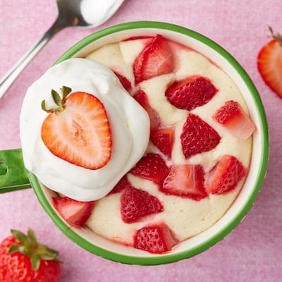 Top-down view of strawberry shortcake mug cake with fresh strawberries and whipped cream on top.