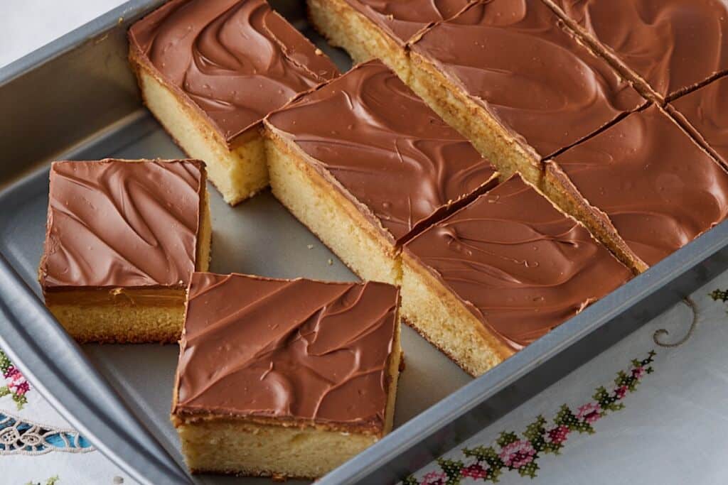 Squares of Tandy Cake in the baking pan, with layers of sponge cake, peanut butter, and chocolate.