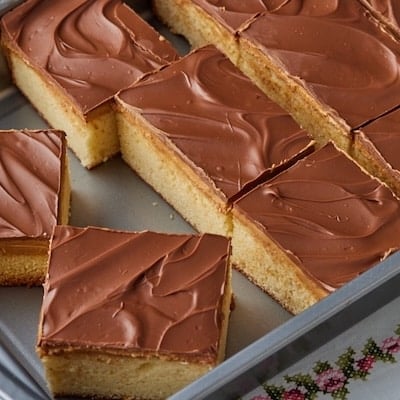 Squares of Tandy Cake in the baking pan, with layers of sponge cake, peanut butter, and chocolate.