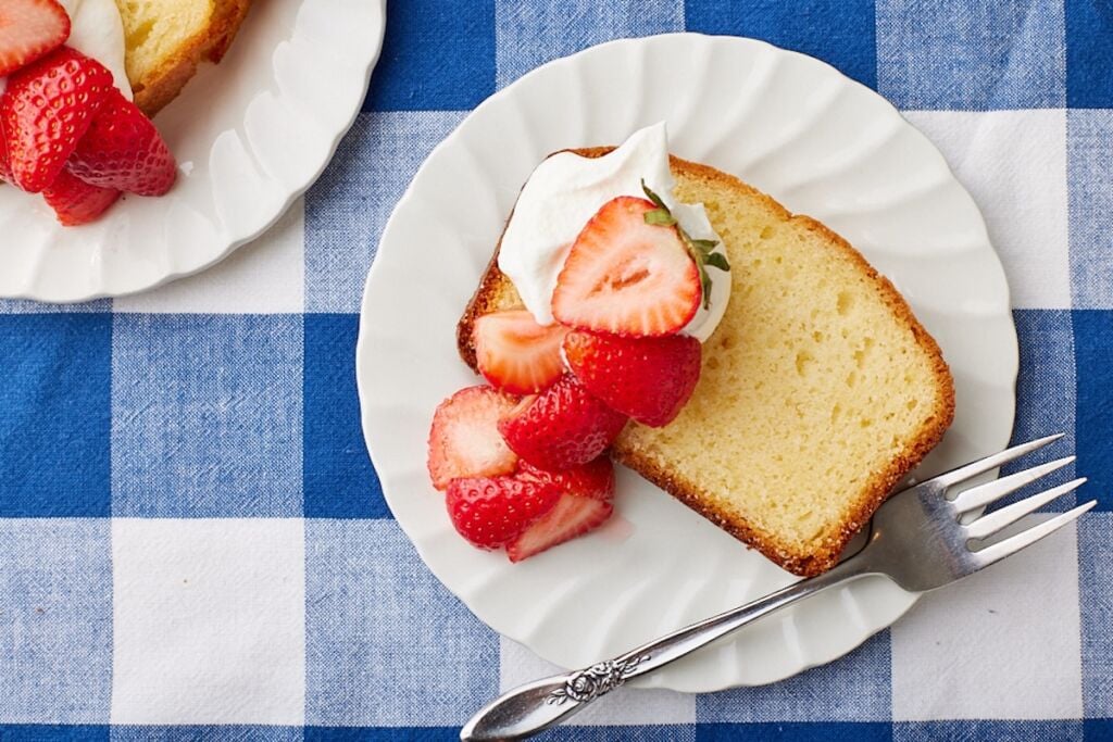 Two slices of French Yogurt Cake are served with whipped cream and fresh strawberry slices on top.