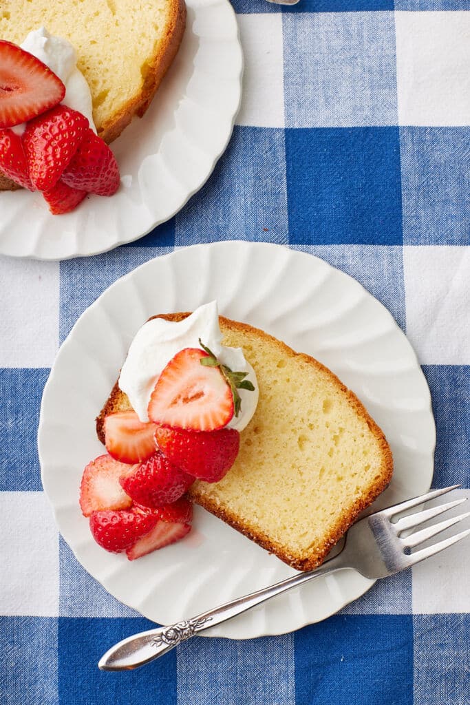 Top-down view of two slices of French Yogurt Cake served with whipped cream and fresh strawberry slices on top.