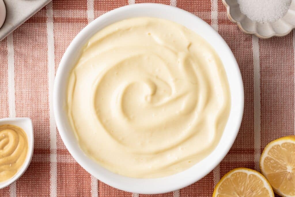 Top-dow view of a bowl of Homemade Mayonnaise with dijon mustard, lemon, egg and salt on the side.