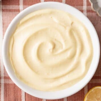 Top-dow view of a bowl of Homemade Mayonnaise with dijon mustard, lemon, egg and salt on the side.
