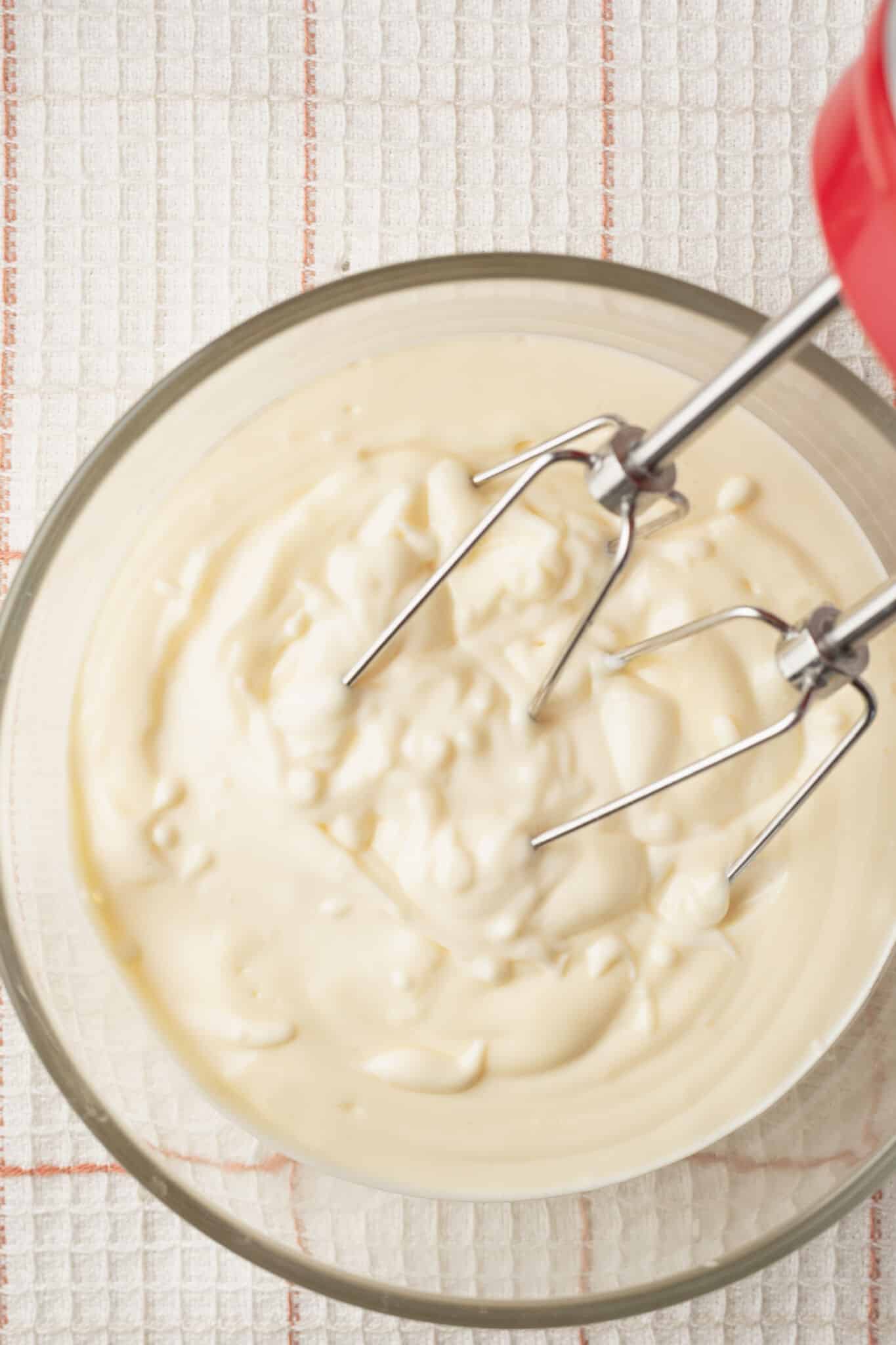 Top-down view of a bowl of mayonnaise made with a handheld mixer.