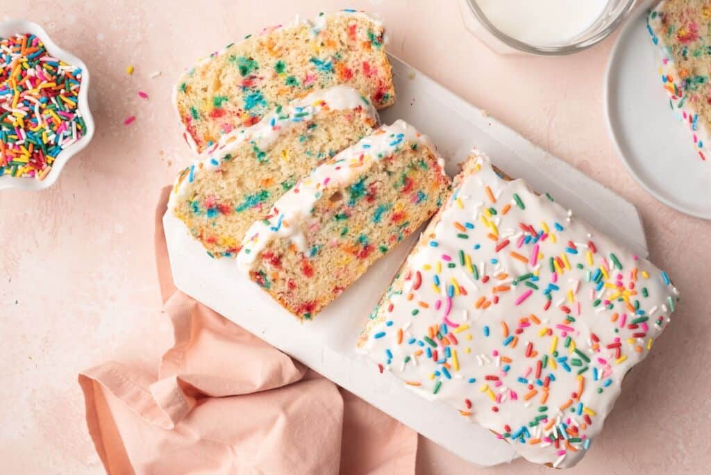 Ice Cream Bread with half loaf sliced into three slices. It's covered with icing and has sprinkle in the crumb and icing.