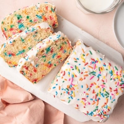 Ice Cream Bread with half loaf sliced into three slices. It's covered with icing and has sprinkle in the crumb and icing.