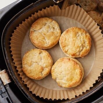 Four golden Air Fryer Scones nestled in a parchment-lined air fryer basket, with crisp tops and tender, flaky centers.