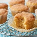 Apple cider muffins with cinnamon-sugar tops, one muffin split open to show its soft, tender crumb, arranged on a wire cooling rack.