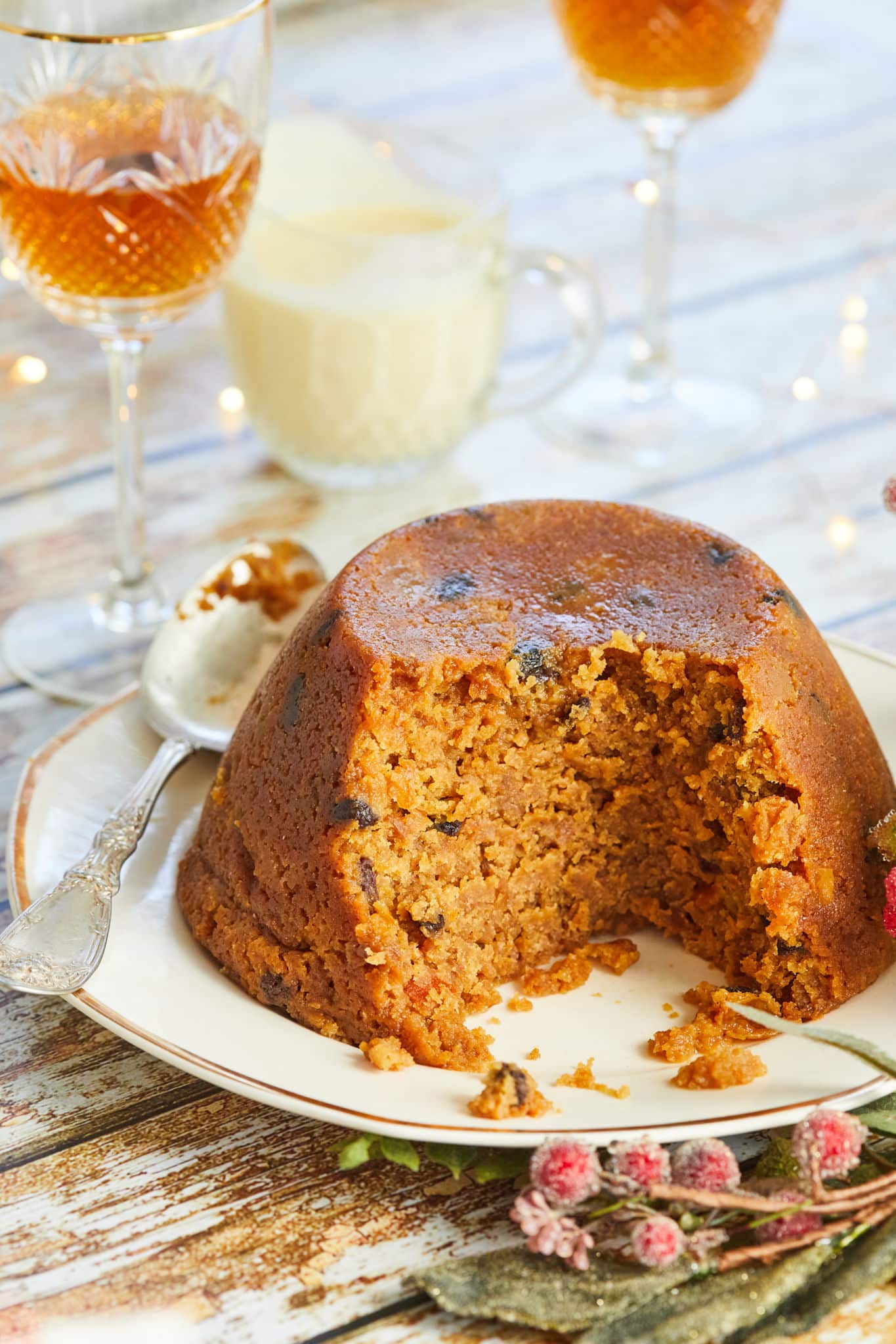 BBB1011207054-scaled Mincemeat pudding with a rich, moist interior studded with dried fruit, served on a white plate with a spoon and festive table decorations.