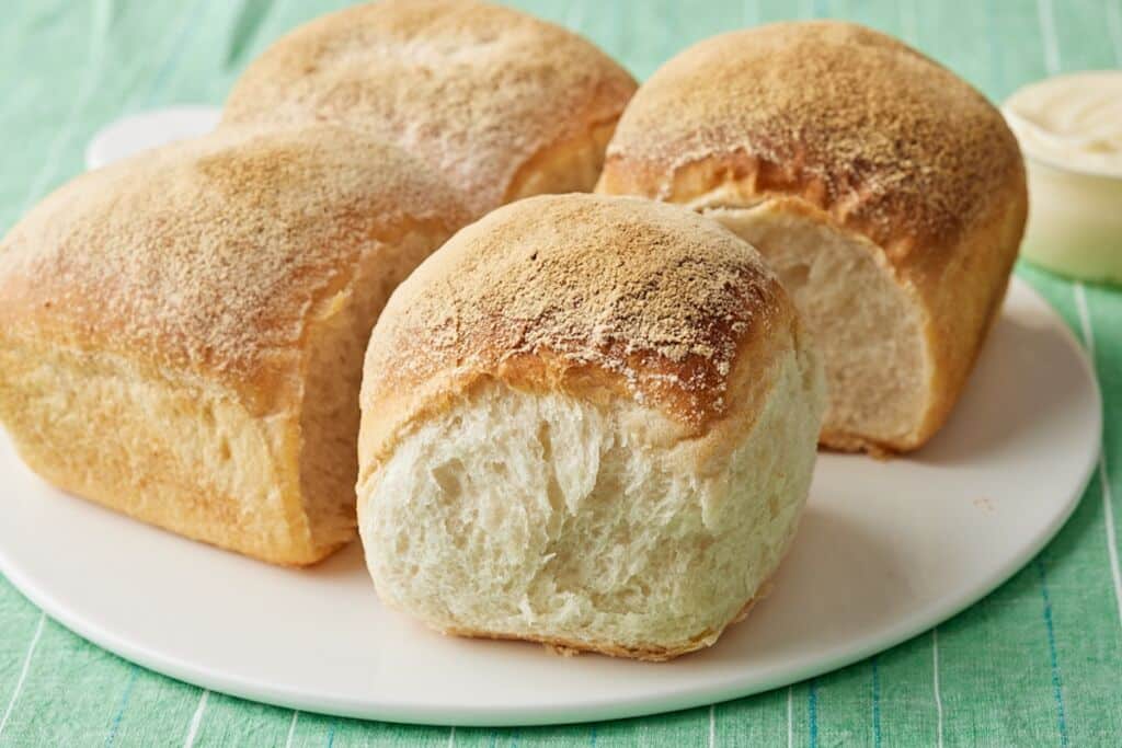 Irish batch bread with four golden-brown loaves baked together, showing soft, airy interiors and lightly floured crusts on a white plate.