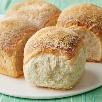 Irish batch bread with four golden-brown loaves baked together, showing soft, airy interiors and lightly floured crusts on a white plate.