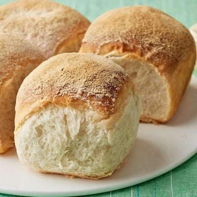 Irish batch bread with four golden-brown loaves baked together, showing soft, airy interiors and lightly floured crusts on a white plate.