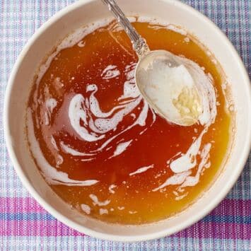 A bowl of golden-brown melted butter with browned milk solids and a spoon.