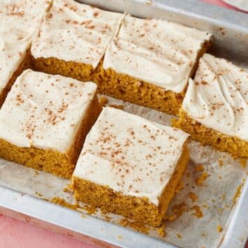 Pumpkin spice cake with cream cheese frosting, dusted with cinnamon and cut into squares in a baking pan.