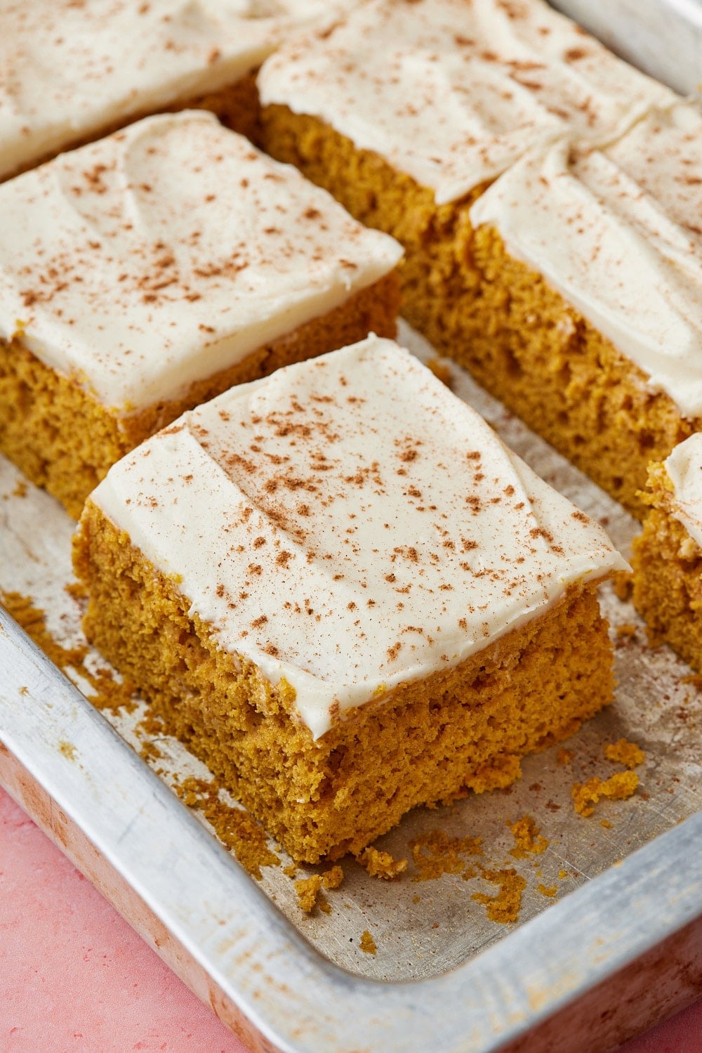 Pumpkin Spice Cake w Cake Mix5 Close-up of pumpkin spice cake squares topped with creamy cream cheese frosting and a sprinkle of cinnamon, showing the moist, tender crumb.