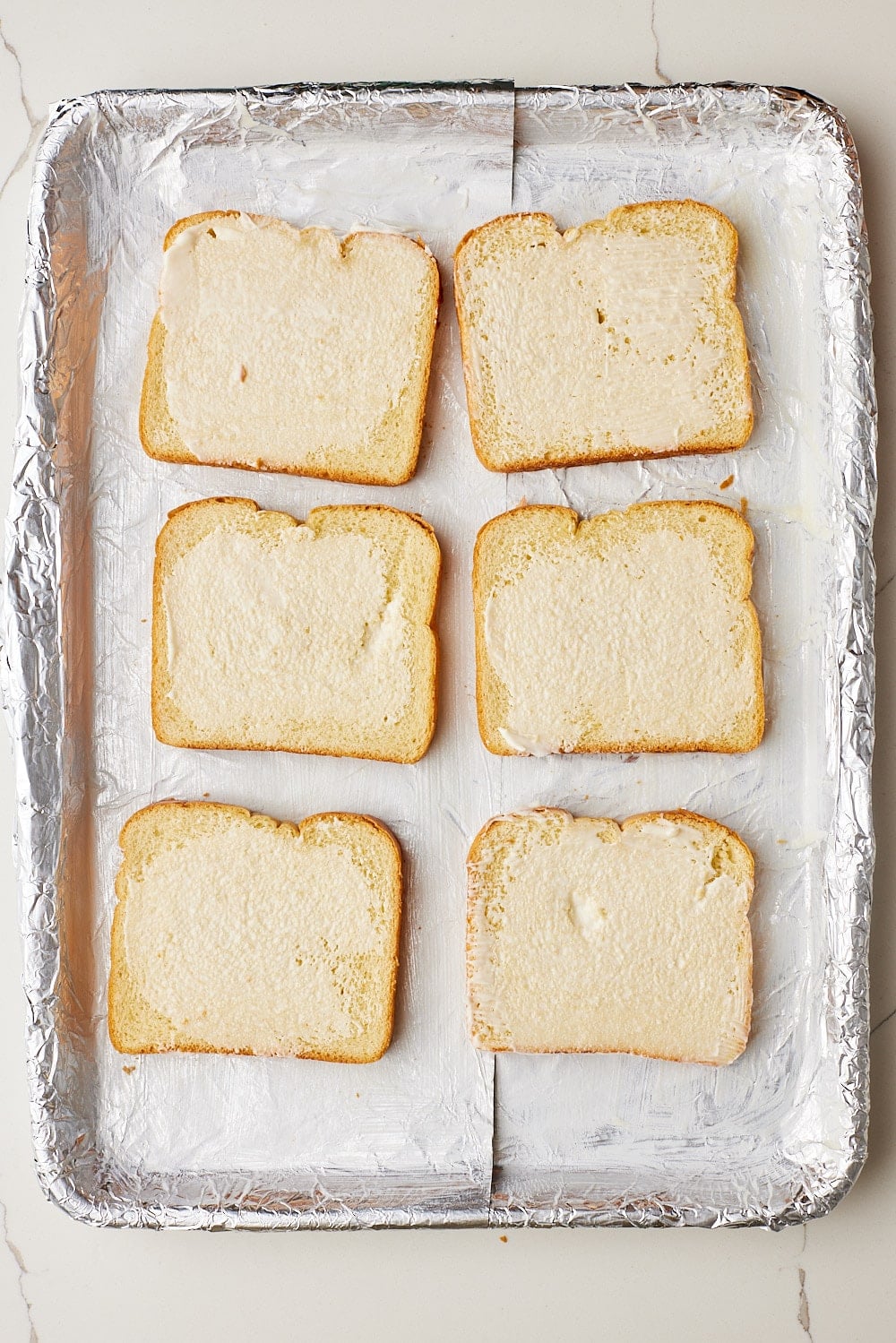 Sheet Pan French Toast2 Buttered brioche slices arranged on a foil-lined sheet pan, ready to make Sheet Pan French Toast.