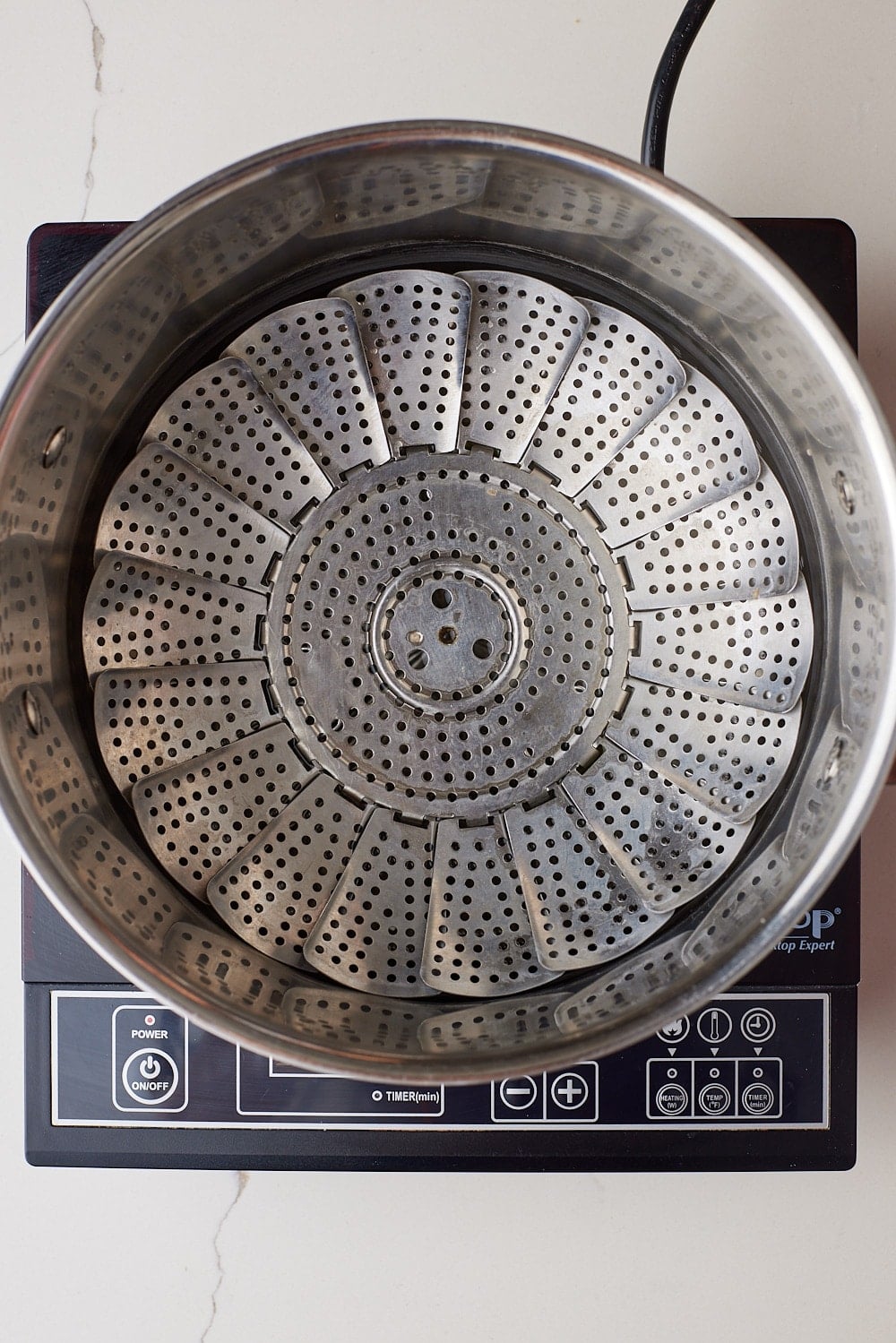Spotted Dick3 Stainless steel steamer basket in a pot, set up for steaming on a stovetop.
