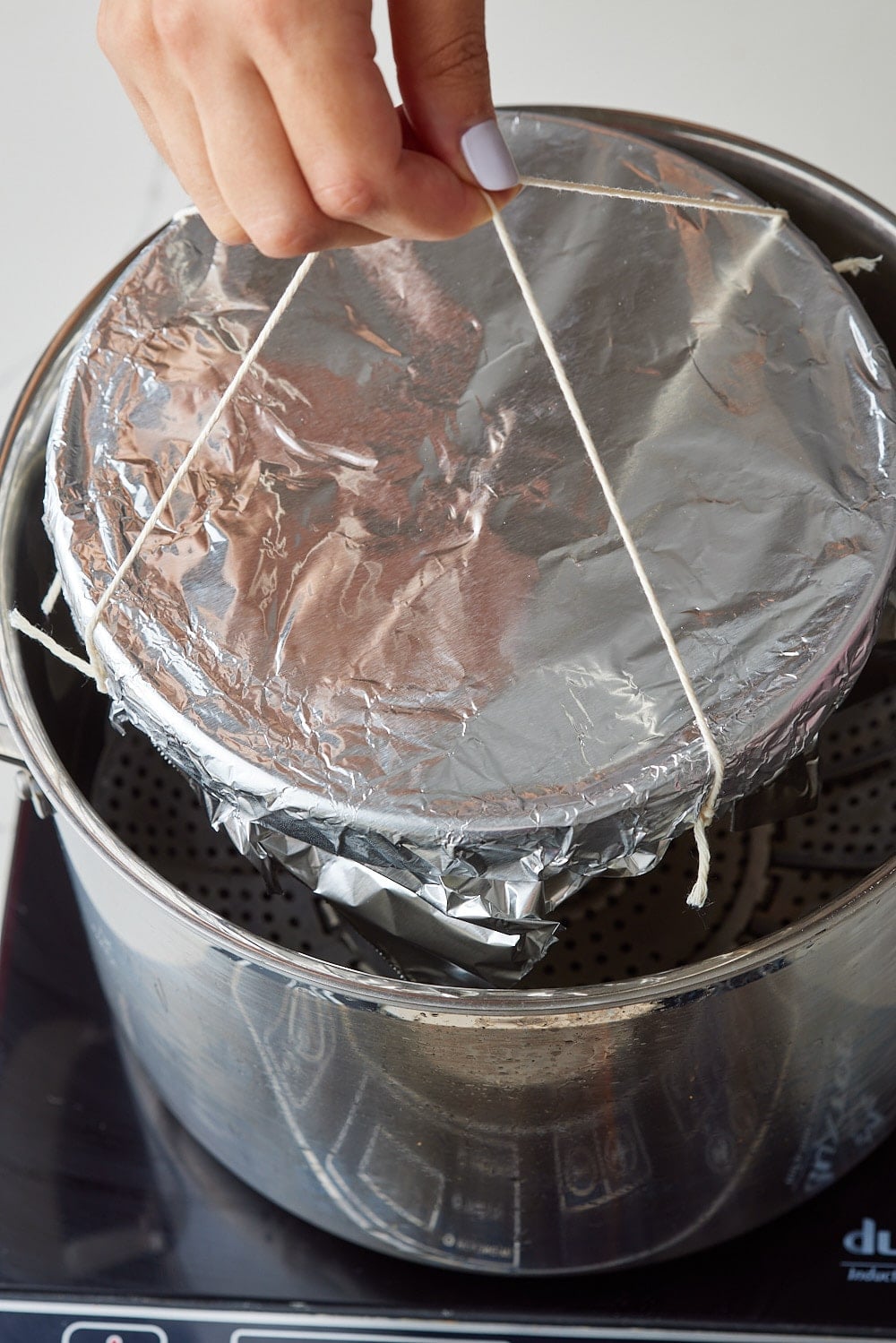 Spotted Dick9 Hands tying twine around a foil-covered pudding basin before steaming in a pot.