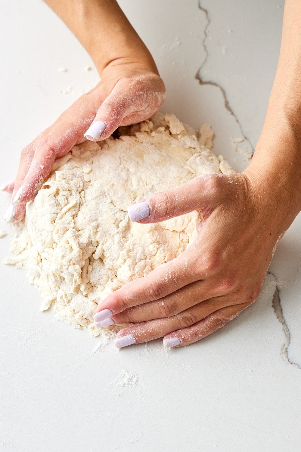 Air Fryer Scones3 Hands gently bringing the crumbly scone dough together on a lightly floured countertop, ready to shape and cut into scones.
