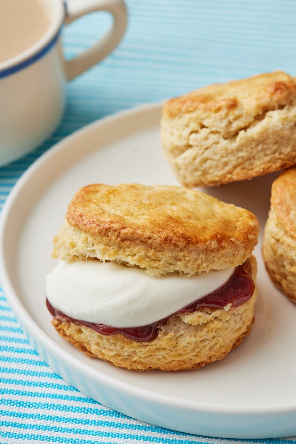 Air Fryer Scones8 Golden, flaky Air Fryer Scones filled with sweet raspberry jam and whipped cream, served on a plate with extra scones and a cup of tea.