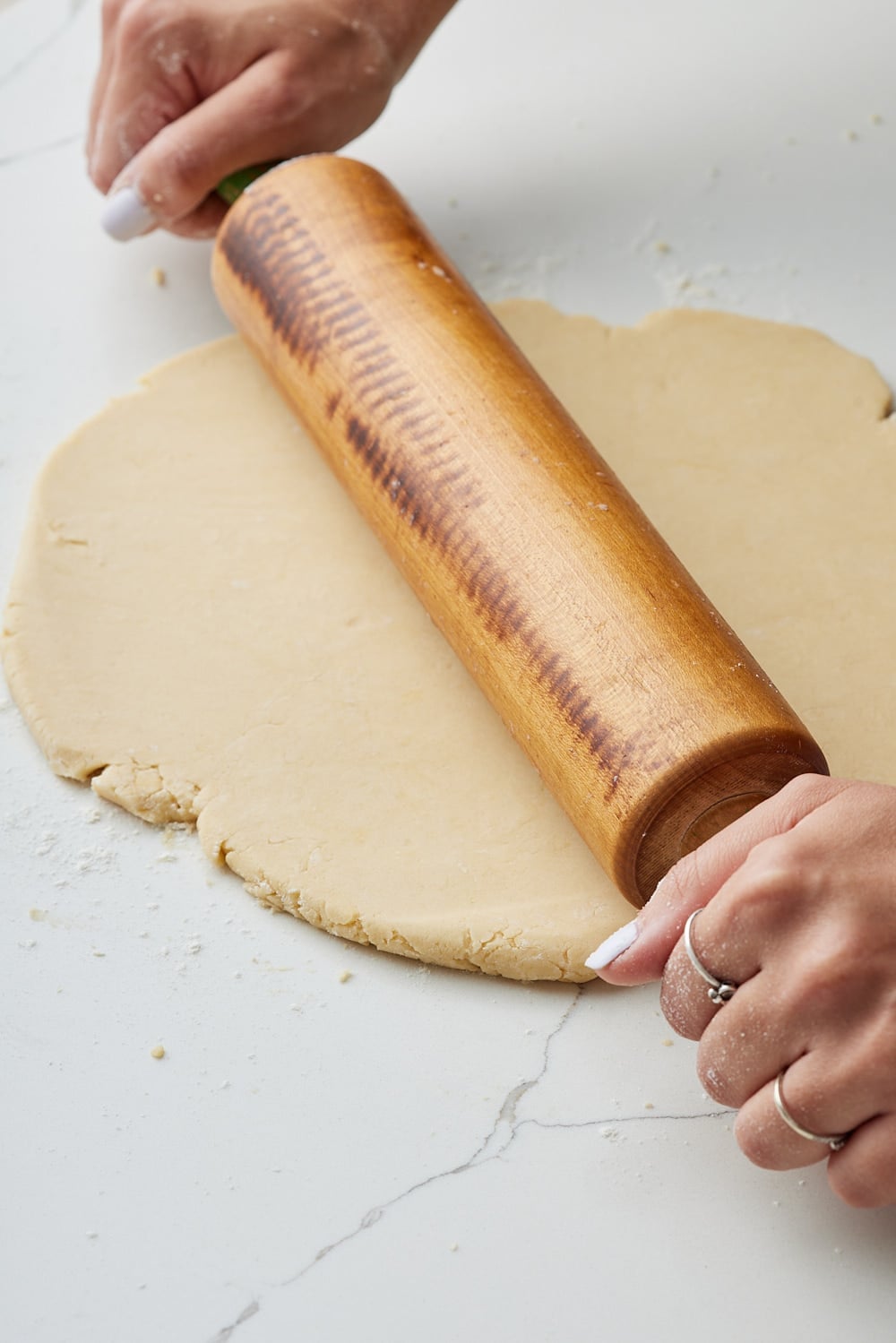 Rolling out homemade brown butter pie dough with a wooden rolling pin on a lightly floured marble countertop. 