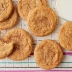 Brown butter snickerdoodle cookies with a cinnamon-sugar coating arranged on a wire cooling rack, with a glass of milk beside them.