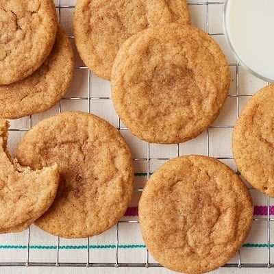 Brown butter snickerdoodle cookies with a cinnamon-sugar coating arranged on a wire cooling rack, with a glass of milk beside them.