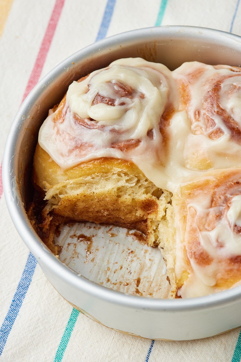 Small Batch Cinnamon Rolls17 Small-batch cinnamon rolls freshly baked in a round pan and topped with creamy icing, with one roll removed.