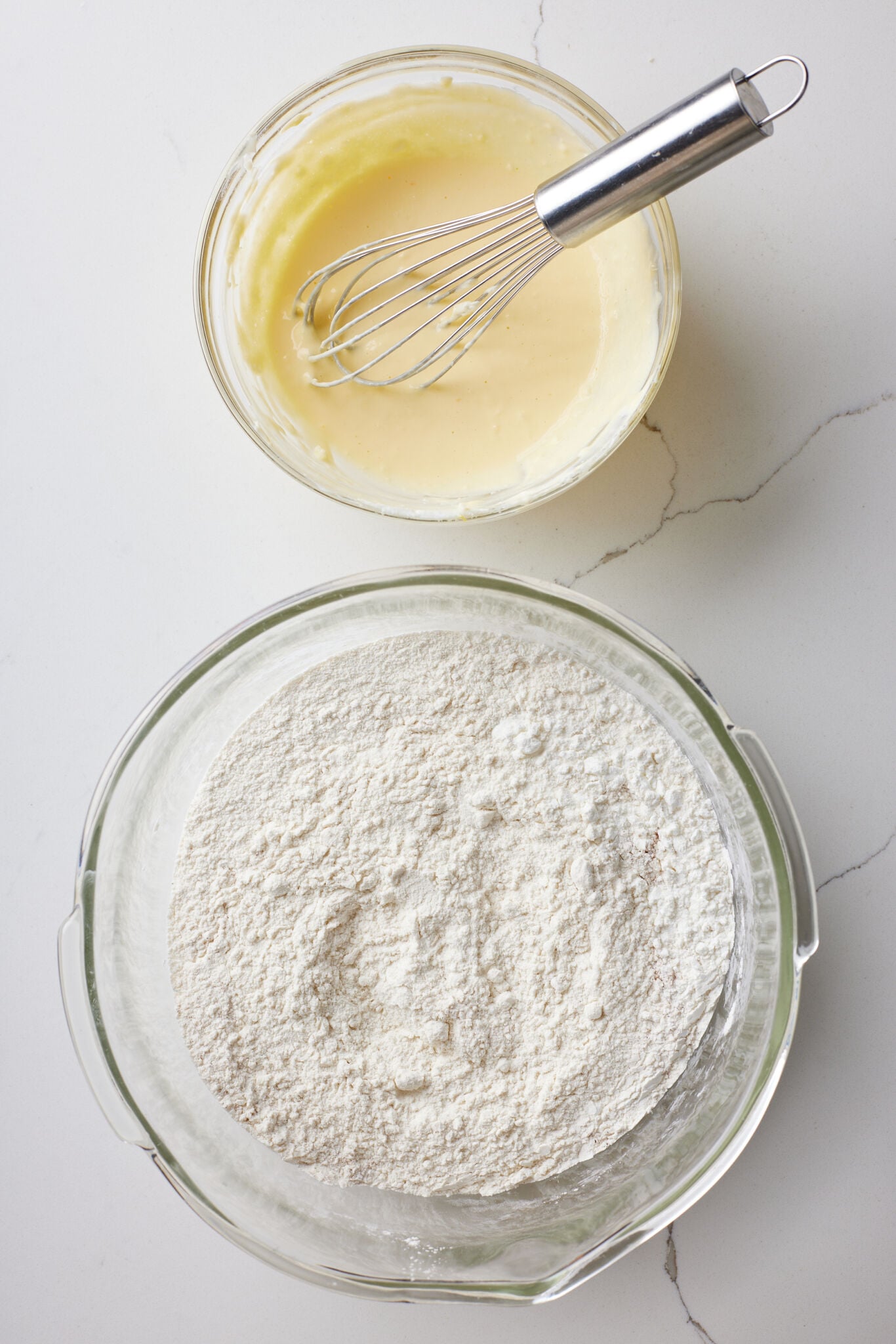 Small Batch Cinnamon Rolls2 Two bowls of ingredients for small-batch cinnamon rolls, with a whisk in the bowl of wet ingredients and flour in a separate bowl.