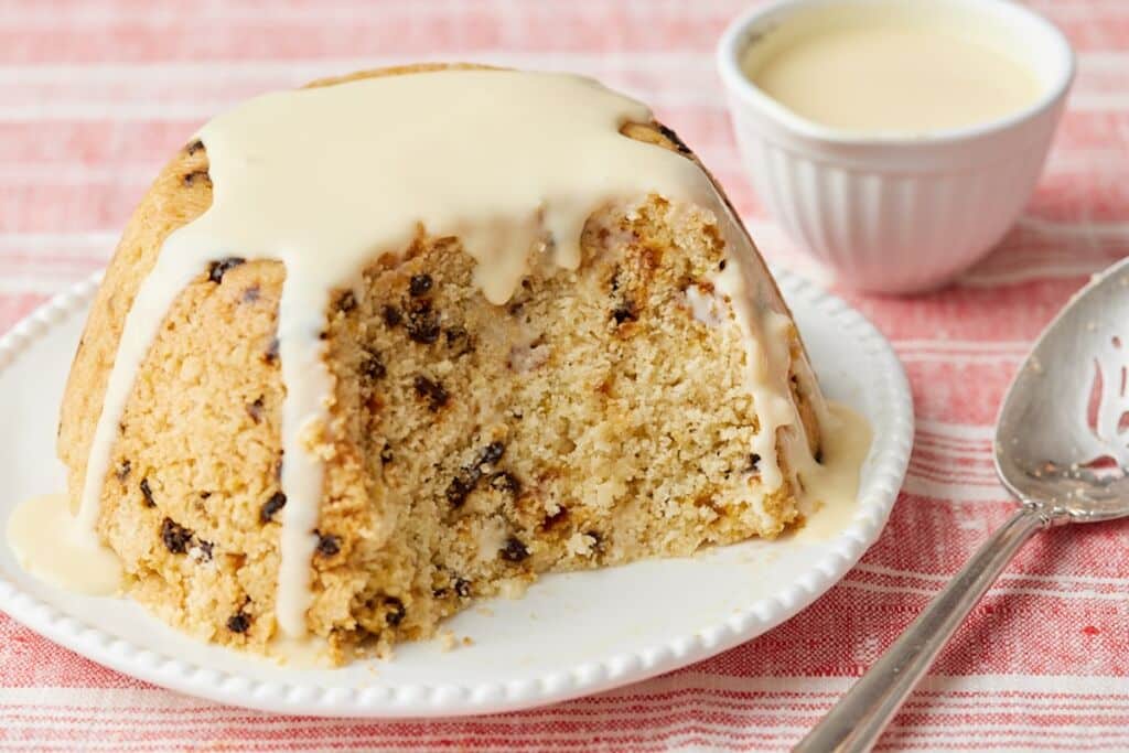 Spotted Dick steamed pudding with currants, topped with custard and served warm.